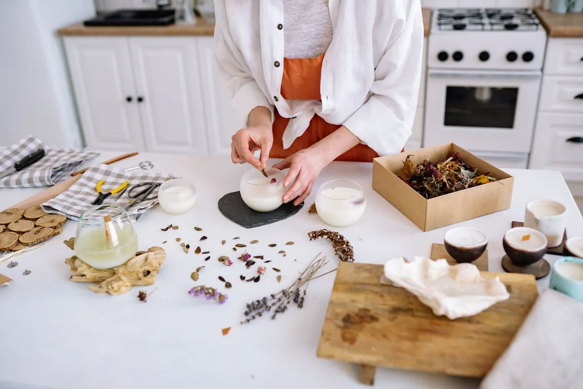 Maker adding dried flowers to handmade candles at a kitchen table