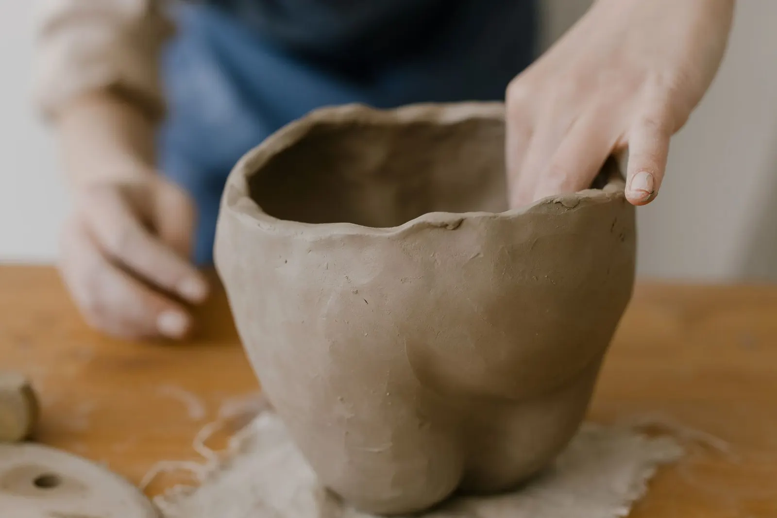 Hands shaping a clay pot at a wooden workbench